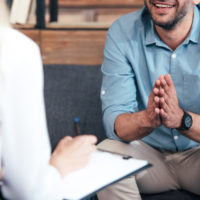 cropped image of female counselor writing in clipboard and smiling male holding hand palms together during therapy session in office cropped image of female counselor writing in clipboard and smiling male holding hand palms together during therapy session in office