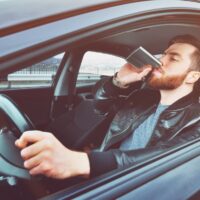 A drunken man driving a car with a bottle of alcohol in his hand. Man whiskey from an iron flask behind the wheel of a car