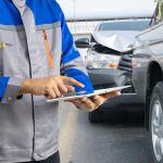 Insurance officer writing clipboard and examining check for damage car after accident.