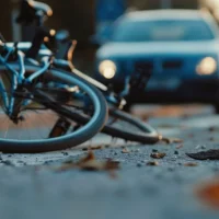 A fallen bicycle lies on the road with a car approaching in the background. The scene captures a moment of potential danger and road safety awareness. A fallen bicycle lies on the road with a car approaching in the background. The scene captures a moment of potential danger and road safety awareness.